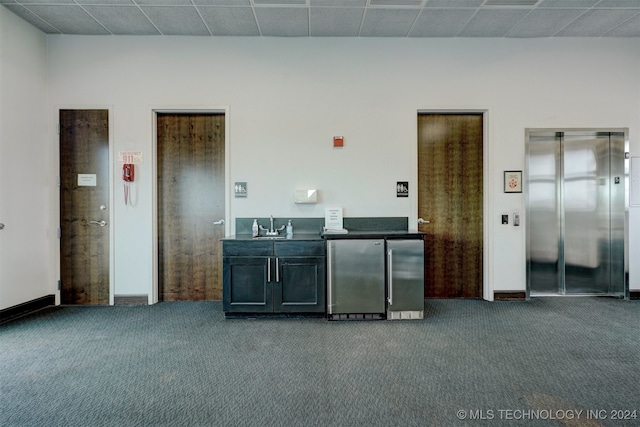 bar featuring dark carpet, elevator, sink, and stainless steel refrigerator