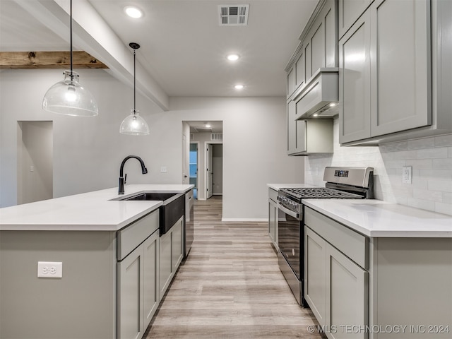 kitchen featuring a center island with sink, light wood-type flooring, stainless steel stove, gray cabinets, and hanging light fixtures