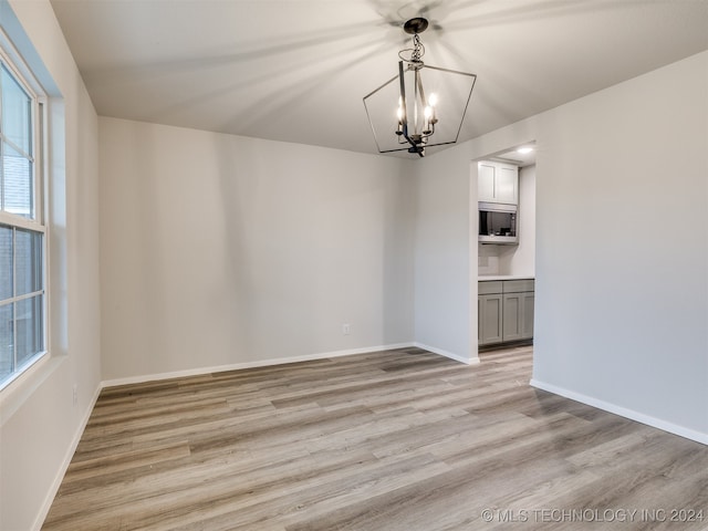 unfurnished dining area with light wood-type flooring, plenty of natural light, and an inviting chandelier