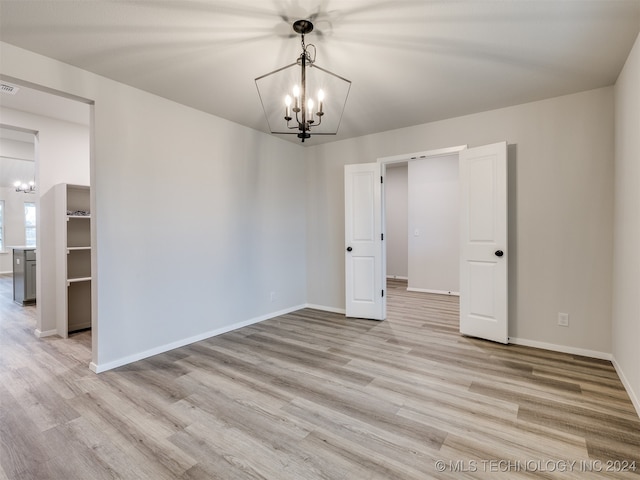 unfurnished room featuring light wood-type flooring and an inviting chandelier