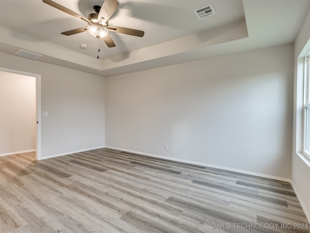 unfurnished room featuring light wood-type flooring, ceiling fan, and a raised ceiling