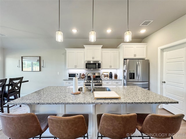 kitchen featuring white cabinets, a kitchen island with sink, stainless steel appliances, and hanging light fixtures