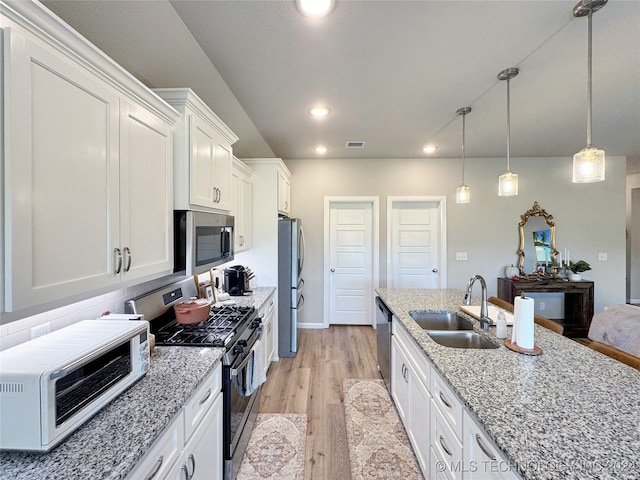 kitchen featuring light wood-type flooring, stainless steel appliances, sink, hanging light fixtures, and white cabinetry