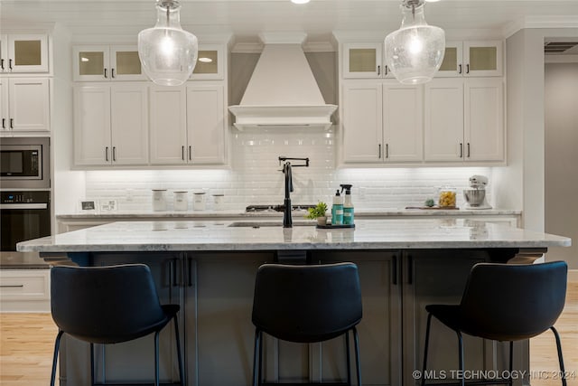 kitchen featuring a kitchen island with sink, stainless steel appliances, and custom range hood