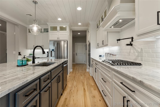 kitchen featuring light wood-type flooring, white cabinets, custom range hood, stainless steel appliances, and decorative light fixtures