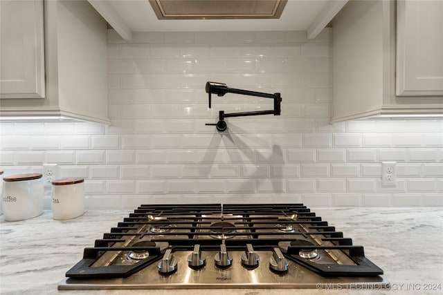 interior details featuring stainless steel gas stovetop, beamed ceiling, backsplash, and light stone counters