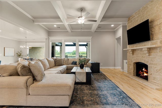 living room with coffered ceiling, ceiling fan with notable chandelier, a stone fireplace, beam ceiling, and hardwood / wood-style floors