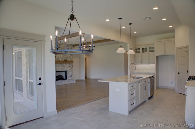 kitchen with an inviting chandelier, decorative light fixtures, a center island with sink, stainless steel dishwasher, and sink