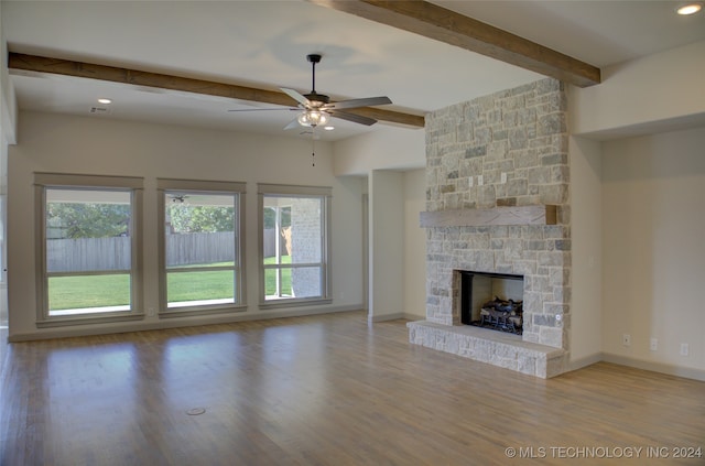 unfurnished living room featuring light hardwood / wood-style flooring, ceiling fan, beamed ceiling, and a stone fireplace