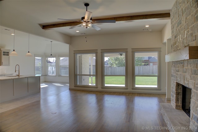 unfurnished living room featuring a stone fireplace, beam ceiling, ceiling fan, hardwood / wood-style floors, and sink