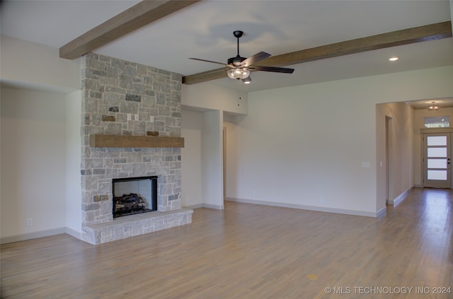 unfurnished living room with ceiling fan, a fireplace, light wood-type flooring, and beam ceiling