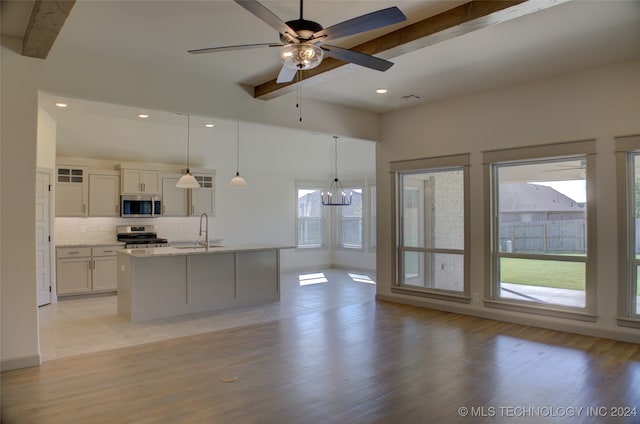 kitchen featuring light wood-type flooring, hanging light fixtures, beam ceiling, appliances with stainless steel finishes, and ceiling fan with notable chandelier