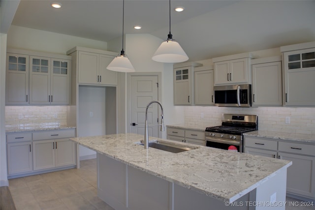 kitchen with pendant lighting, tasteful backsplash, a kitchen island with sink, appliances with stainless steel finishes, and light stone countertops