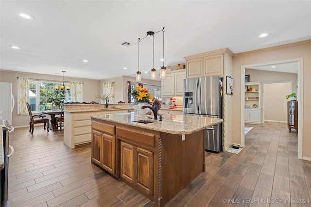 kitchen featuring sink, stainless steel fridge, hanging light fixtures, and an island with sink