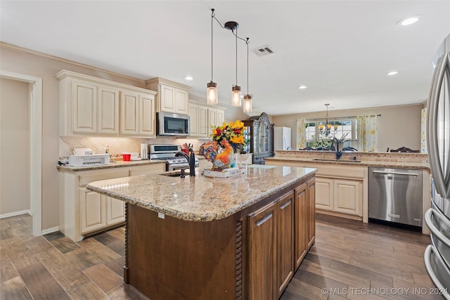 kitchen with appliances with stainless steel finishes, dark hardwood / wood-style flooring, an island with sink, sink, and hanging light fixtures