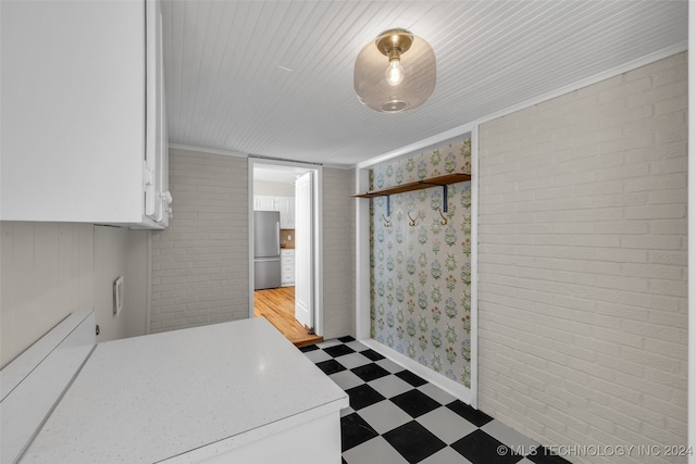 kitchen with stainless steel fridge, white cabinets, ornamental molding, and brick wall