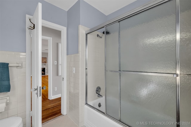 bathroom featuring tile walls, tile patterned flooring, toilet, and bath / shower combo with glass door