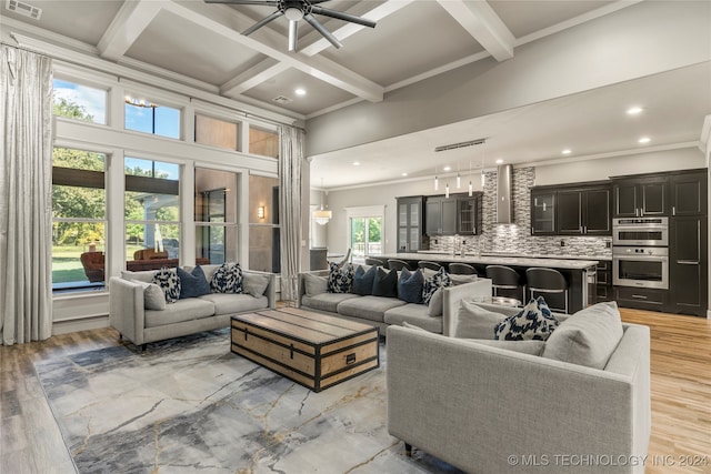 living room with coffered ceiling, ceiling fan with notable chandelier, crown molding, a wealth of natural light, and beam ceiling