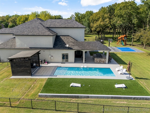 view of swimming pool featuring a playground, exterior kitchen, a patio area, and a yard