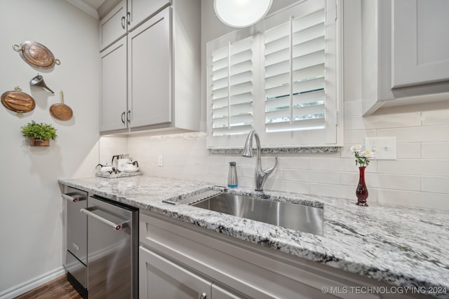 kitchen with dark hardwood / wood-style floors, sink, decorative backsplash, light stone countertops, and stainless steel dishwasher