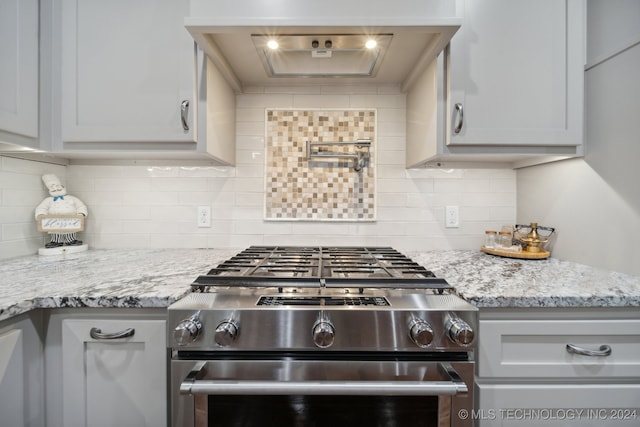 kitchen with stainless steel stove, light stone counters, and backsplash