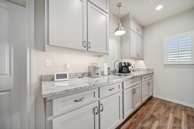 kitchen with light stone counters, white cabinets, hanging light fixtures, sink, and dark hardwood / wood-style floors