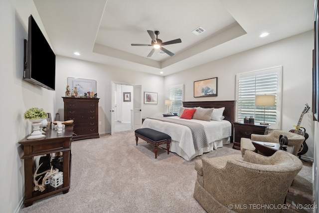 bedroom with light carpet, a raised ceiling, and multiple windows