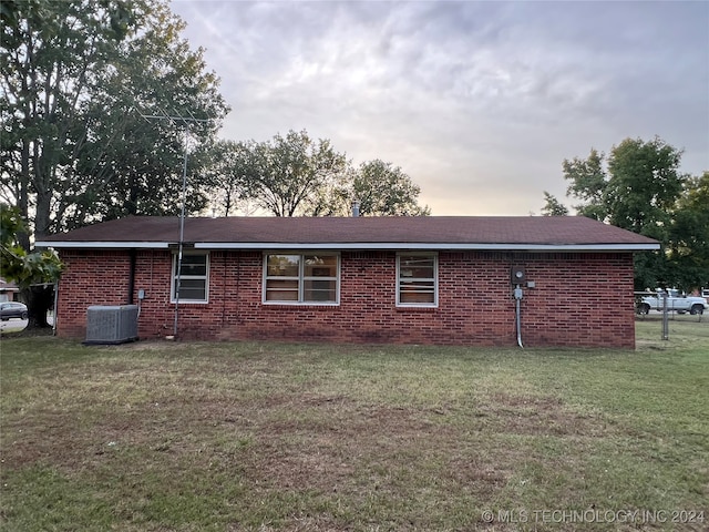 back house at dusk featuring cooling unit and a yard