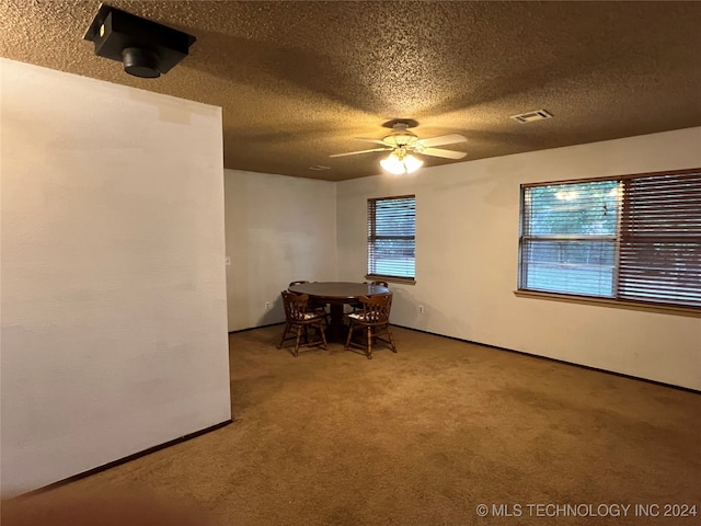 unfurnished dining area with ceiling fan, plenty of natural light, carpet floors, and a textured ceiling