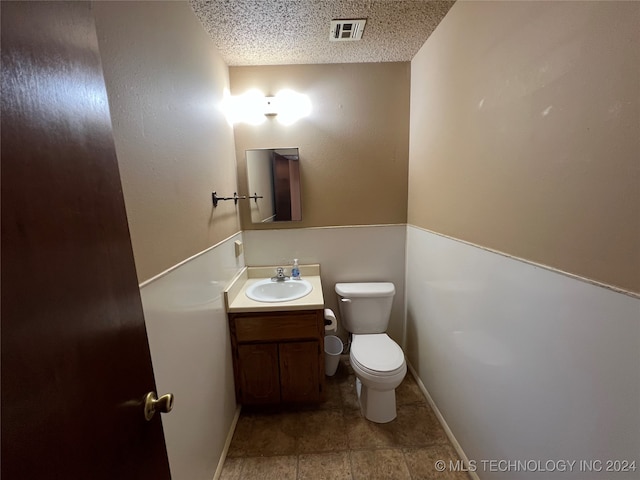 bathroom with a textured ceiling, vanity, and toilet