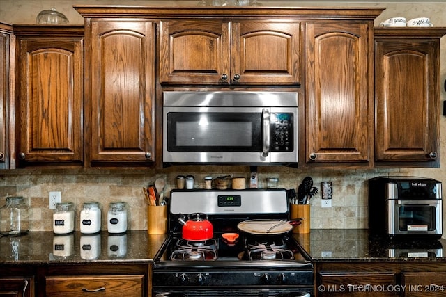 kitchen featuring dark stone countertops, backsplash, and black gas range oven