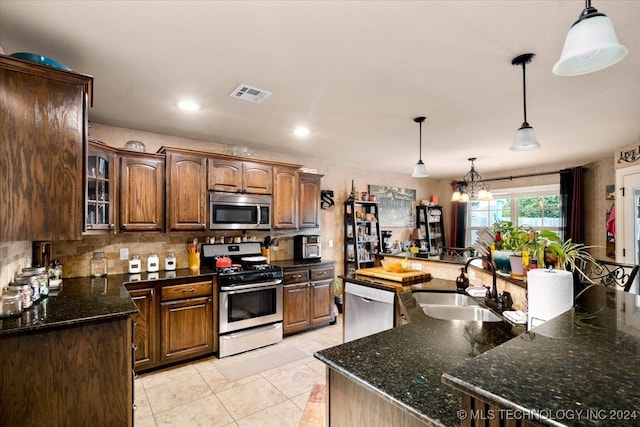 kitchen with appliances with stainless steel finishes, hanging light fixtures, dark stone countertops, sink, and a notable chandelier