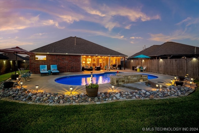 pool at dusk with a lawn, a fire pit, and a patio area