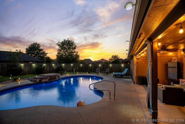 pool at dusk featuring a hot tub, a patio area, and pool water feature