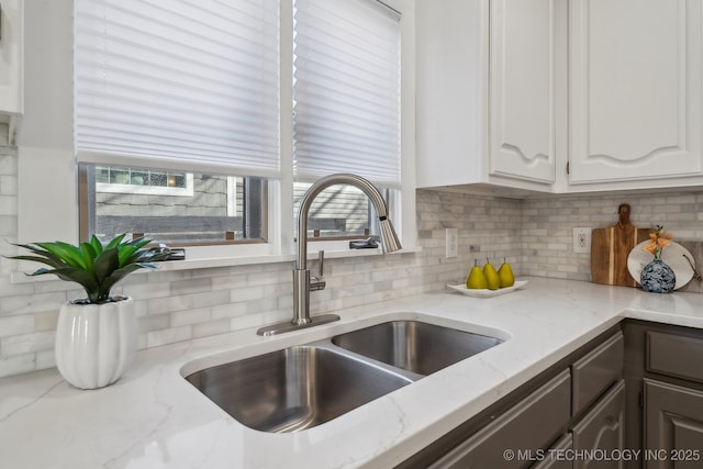 kitchen featuring white cabinetry, light stone counters, backsplash, and a sink