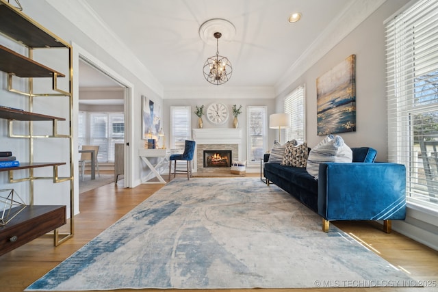 living room with a notable chandelier, a warm lit fireplace, crown molding, and wood finished floors