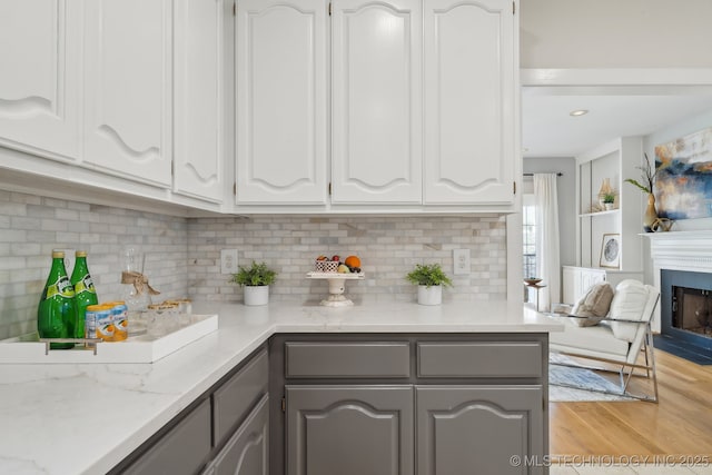 kitchen featuring light wood-style flooring, a fireplace, gray cabinetry, decorative backsplash, and white cabinetry