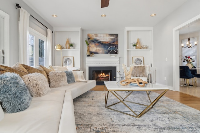 living area featuring recessed lighting, built in features, a warm lit fireplace, and wood finished floors