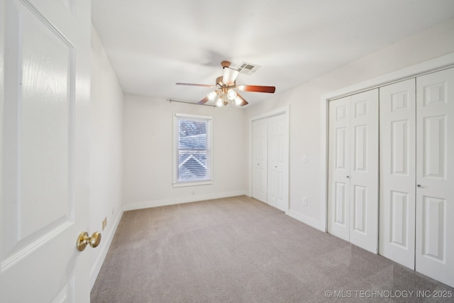 unfurnished bedroom with visible vents, two closets, ceiling fan, baseboards, and carpet floors