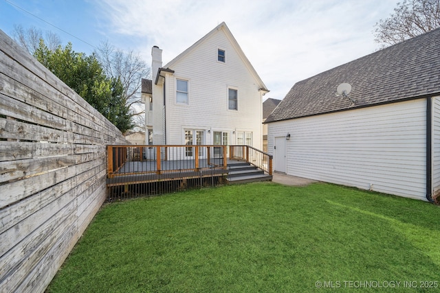 rear view of property with a wooden deck, a lawn, roof with shingles, and a chimney