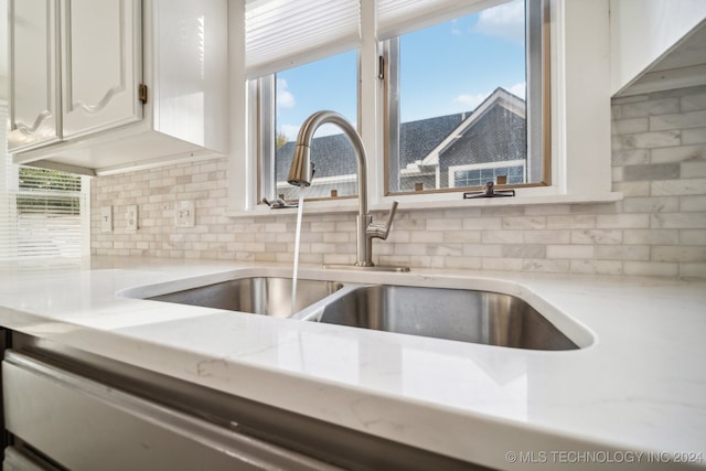 room details with backsplash, light stone counters, white cabinetry, and sink