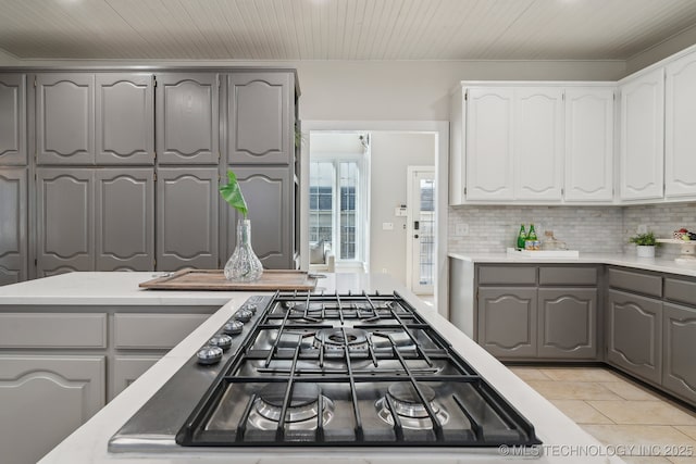 kitchen featuring gray cabinetry, white cabinetry, light tile patterned floors, decorative backsplash, and stainless steel gas cooktop