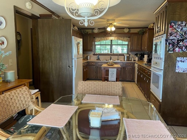 kitchen featuring dark brown cabinetry, ceiling fan, light tile patterned floors, and white appliances