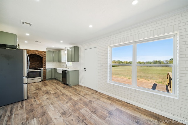 kitchen with stainless steel appliances, green cabinets, light hardwood / wood-style floors, and brick wall