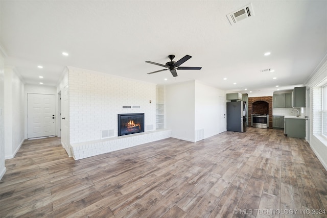 unfurnished living room with light wood-type flooring, crown molding, sink, and ceiling fan