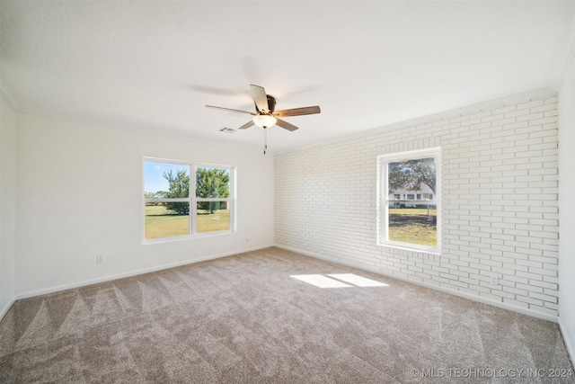 carpeted spare room with brick wall, ornamental molding, ceiling fan, and plenty of natural light