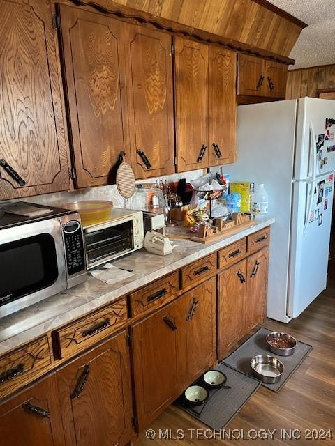 1384 Academy Rd, Bennington, OK 74723 - kitchen with stainless steel microwave, brown cabinetry, light countertops, dark wood-type flooring, and a textured ceiling