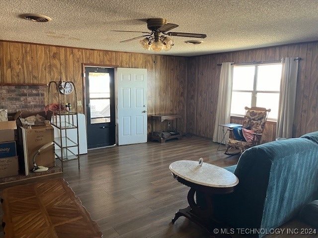 living room with a textured ceiling, ceiling fan, dark hardwood / wood-style floors, and wood walls