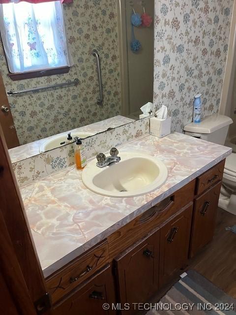 1384 Academy Rd, Bennington, OK 74723 - bathroom with toilet, vanity, wallpapered walls, wood finished floors, and a shower