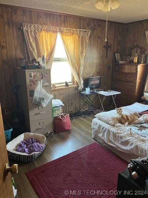 bedroom featuring a textured ceiling, wooden walls, and hardwood / wood-style floors